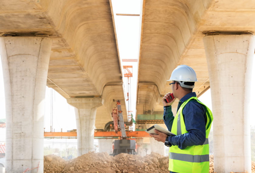 worker doing a digital safety audit checklist under a bridge